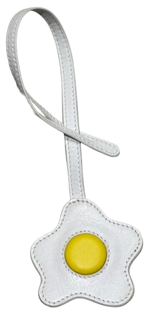 A white faux-leather luggage tag shaped like a fried egg, featuring a white strap and a yellow yolk detail in the center, set against a plain white background.